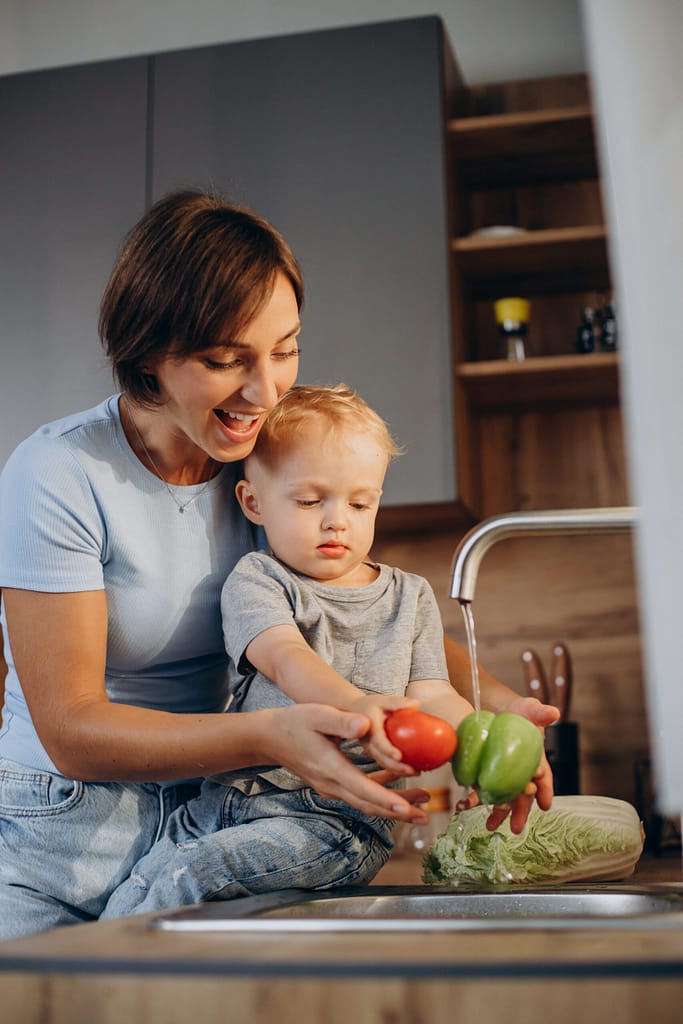 Woman with her son washing vegetables in the kitchen sink